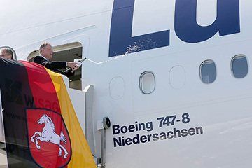 MP Weil auf der Gangway vor der offenen Flugzeugtür beim Schütteln einer Champagnerflasche