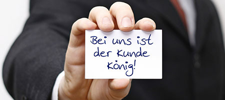 Mann hält ein Kärtchen in die Kamera mit dem Text "Bei uns ist der Kunde König"