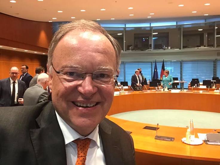 Ein Selfie zeigt Ministerpräsident Stephan Weil vor einem Konferenztisch, im Hintergrund ist Bundeskanzlerin Angela Merkel zu sehen.