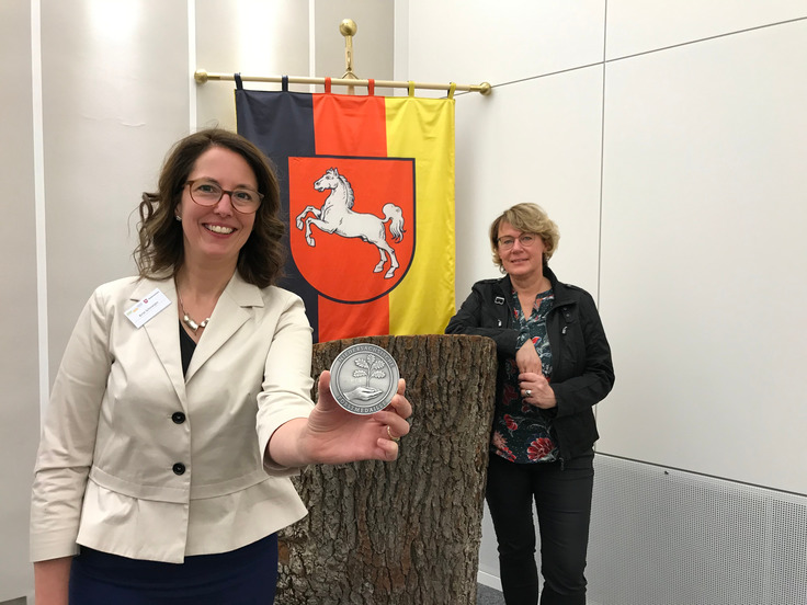 Preisträgerin Birte Schmetjen präsentiert die Niedersächsische Forstmedaille; Ministerin Barbara Otte-Kinast steht im Hintergrund.
