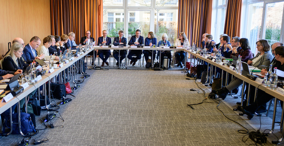 Blick in einen Sitzungsraum mit Tischreihen rechts und links sowie einer Frontreihe, an dem die Kabinettsmitglieders der Niedersächischen Landesregierung sitzen.