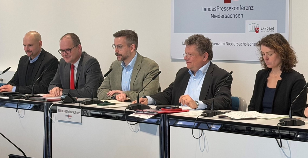 Vier Männer und eine Frau sitzen in einer Reihe und blicken in in den Raum. Im Hintergrund hängt ein Schild an der Wand mit der Aufschrift LandesPressekonferenz Niedersachsen.